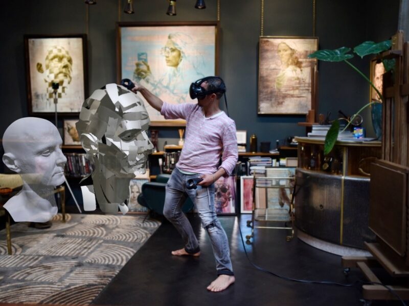A person wears a VR headset in a studio . Screens are on the wall at the back of the room