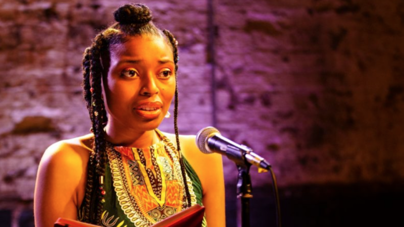 A black woman with braids in front of a microphone performing