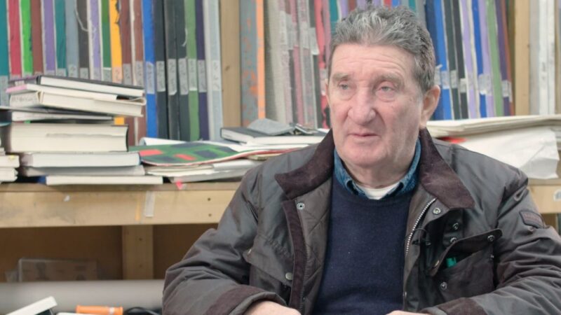 A photograph of an older man in front of a book shelf