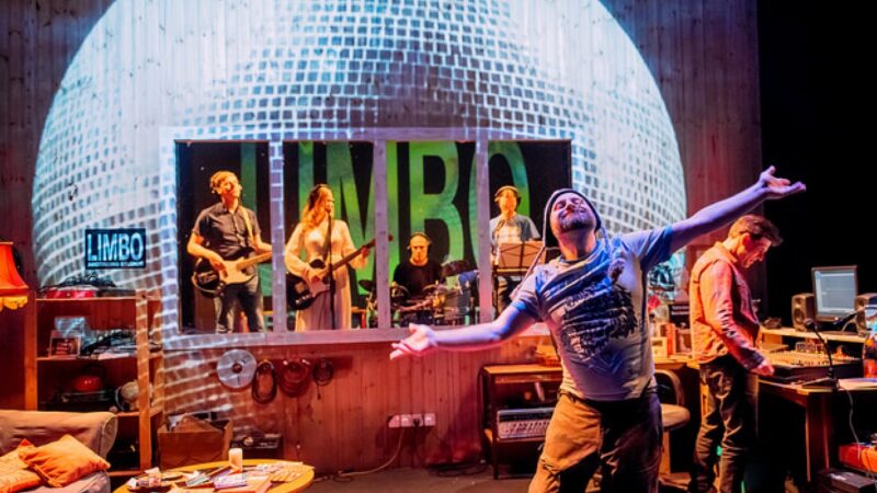 A photo of a band performing inside a large disco ball with a man smoking in front of them