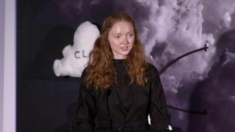 A woman with ginger hair in front of a background with clouds on it