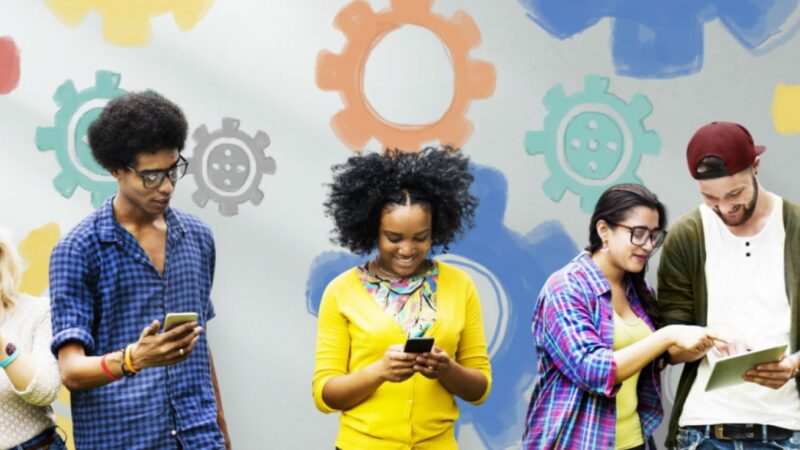Group of people on smartphones and tablets in front of a background with colourful gears