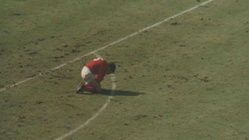 A photograph of a football player collapsed into a ball in the middle of the pitch