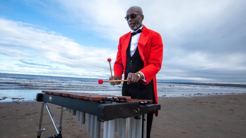 A man in a red waist coat playing the xylophone