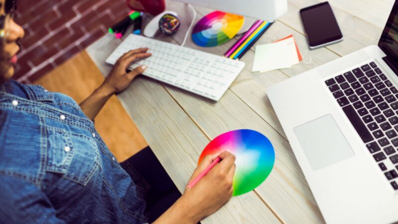 A person with one hand on the keyboard and the other on a colour board