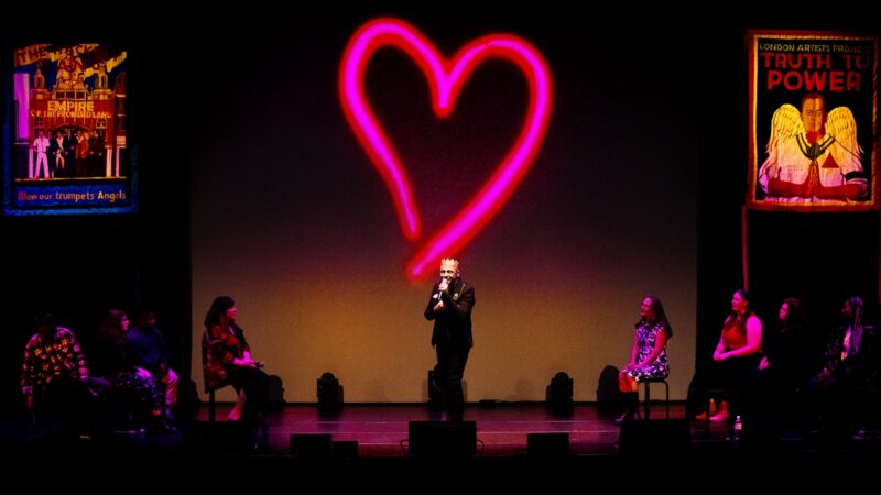 A performance from Truth to Power Cafe with people on stage with a large heart in the background