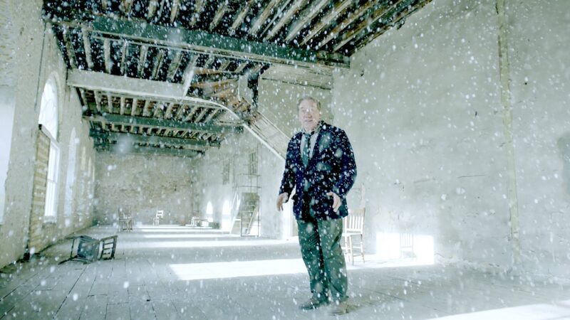 A man standing in an empty white room with snow falling from the roof