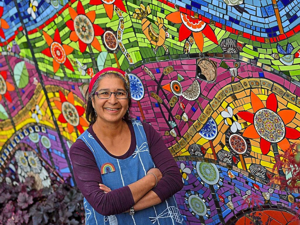 Caroline Jariwala standing in front of a wall of colourful swirling mosaics.