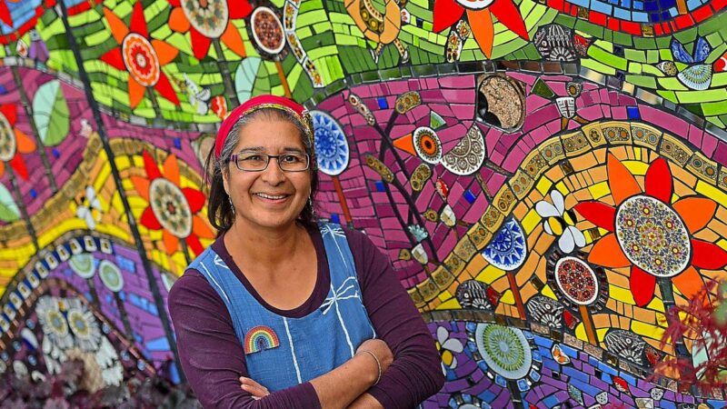 Caroline Jariwala standing in front of a wall of colourful swirling mosaics.
