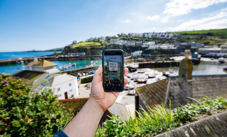 A hand holds a mobile phone. We see a seaside setting in the background