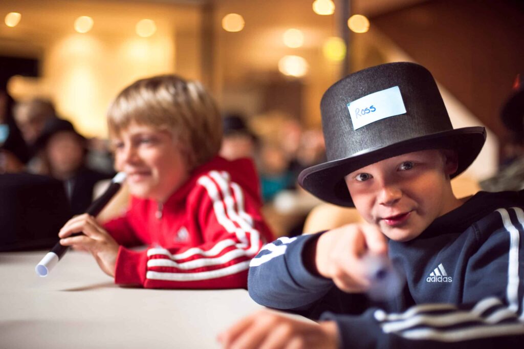 Two young boys sitting at a table with black and white wands and a top hat