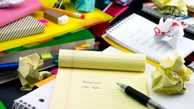 Brightly coloured piles of notebooks and screwed up pieces of paper and stationary on a desk