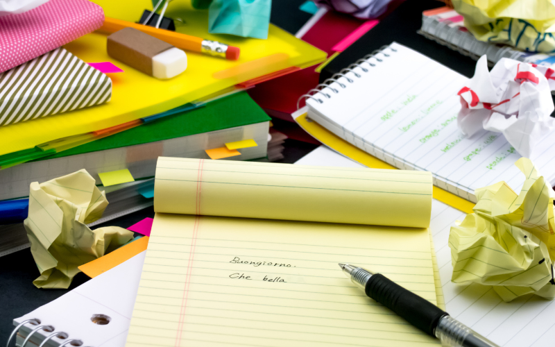Brightly coloured piles of notebooks and screwed up pieces of paper and stationary on a desk