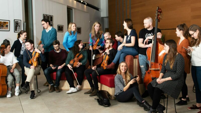 Members of young orchestra sitting toghetr with their instruments and chatting