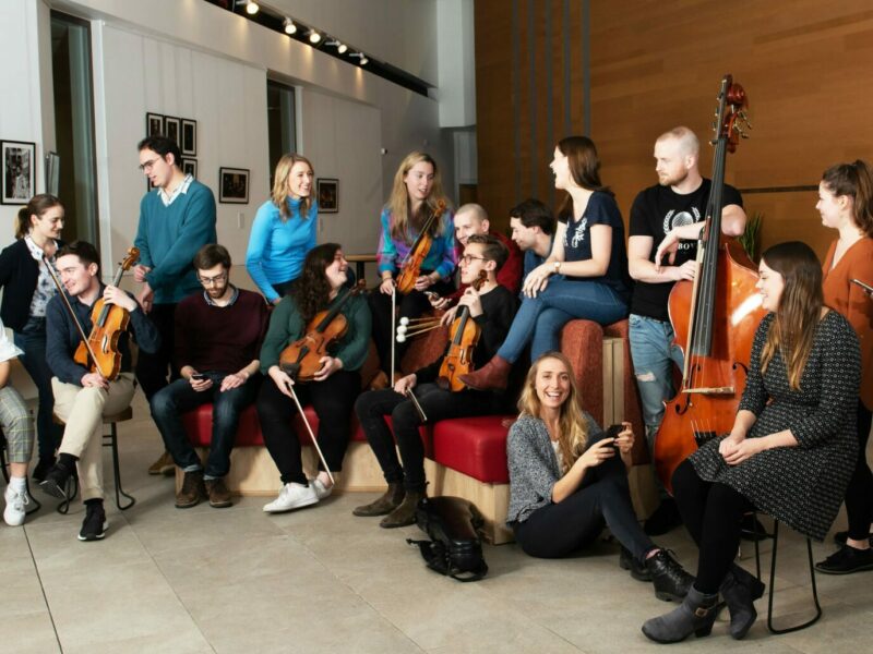 Members of young orchestra sitting toghetr with their instruments and chatting