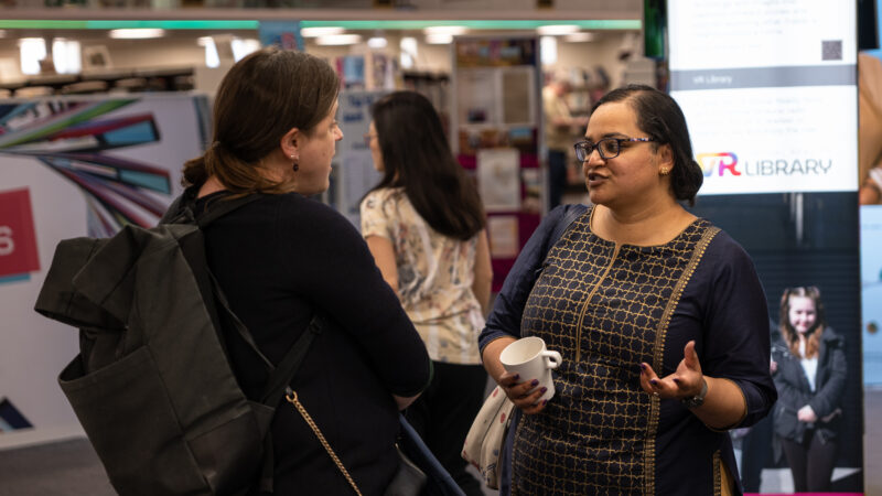 Two women, one white, one south asian talk in a library