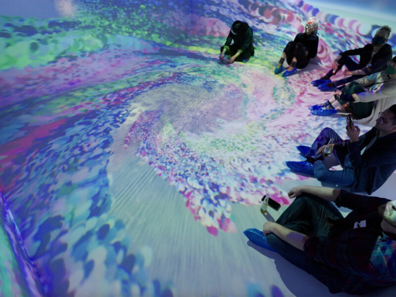 people sit crossed legged on the floor and are surrounded by projections