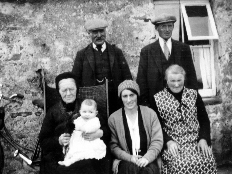Black and white photo of a family with a midwife and baby on Orkney , taken outside their home.