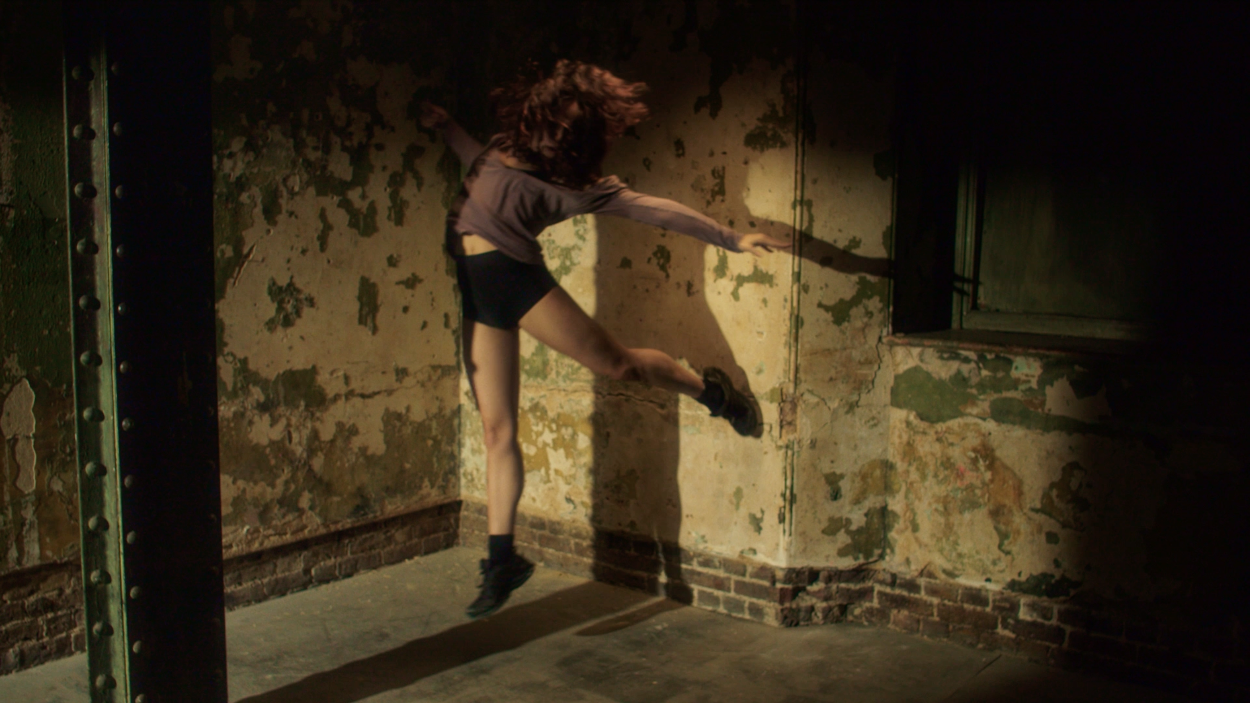 Photo of a dancer in flight against a brick wall with peeling paint.