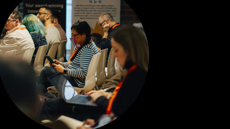 People sit in rows at a conference, looking at their mobile phones