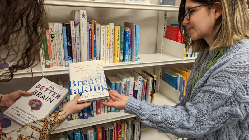 Two people select books from a shelf in a library