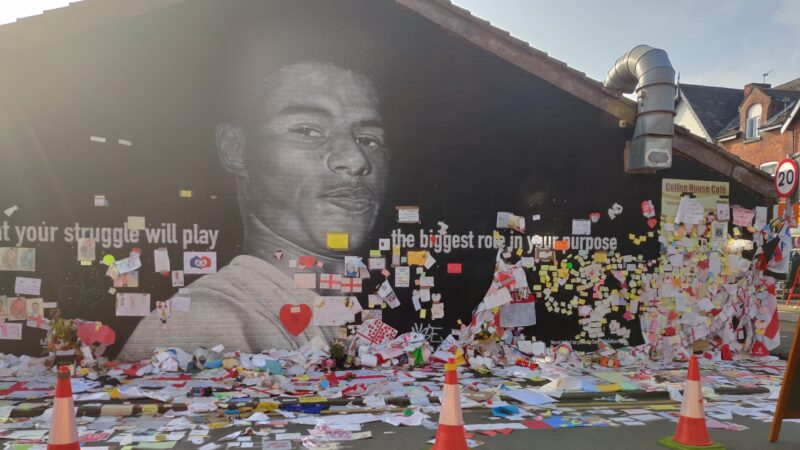 Marcus Rashford Mural. A likeness of footballer Marcus Rashford is painted onto the side of a building. Letters, notes, drawings and messages are pinned onto the mural.