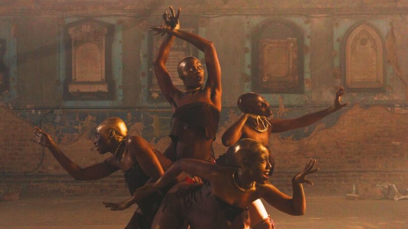 4 otherworldly creatures akin to black women, with golden bald heads, pose amused with arms outstretched sensually upwards, to the left and to the right