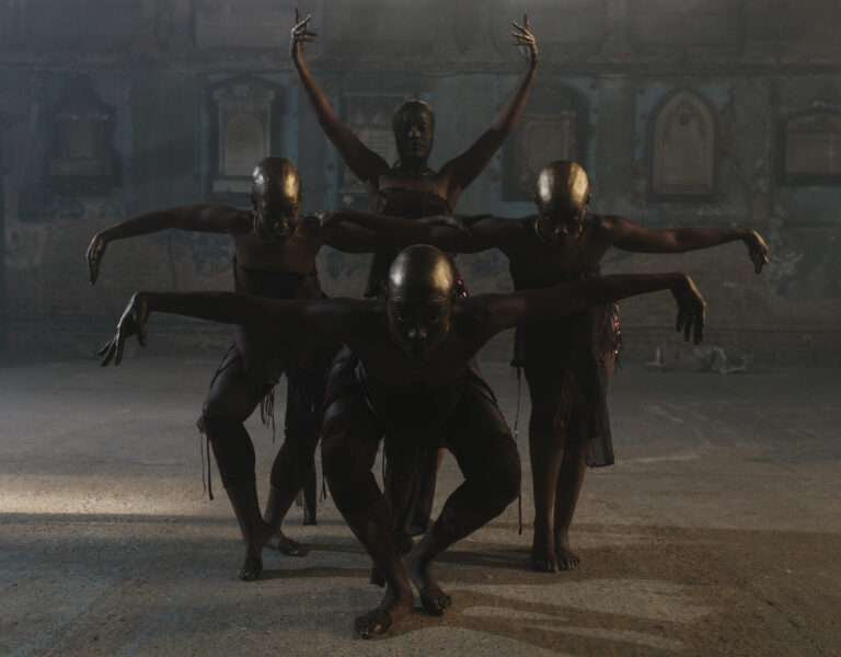4 otherworldly creatures akin to black women, with golden bald heads, pose like crows with arms stretched to either side