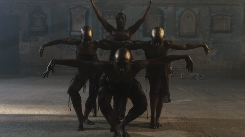 4 otherworldly creatures akin to black women, with golden bald heads, pose like crows with arms stretched to either side