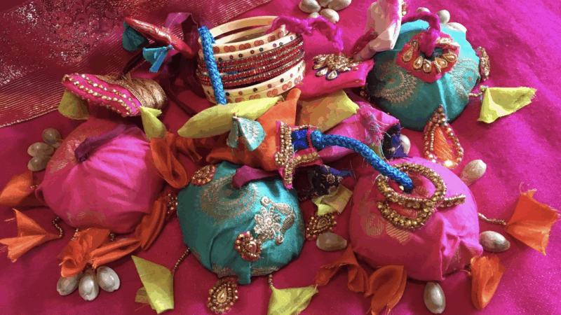 Colorful traditional Indian fabric pouches adorned with gold embroidery, beads, and decorative tassels on a vibrant pink cloth.