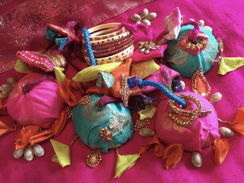 Colorful traditional Indian fabric pouches adorned with gold embroidery, beads, and decorative tassels on a vibrant pink cloth.