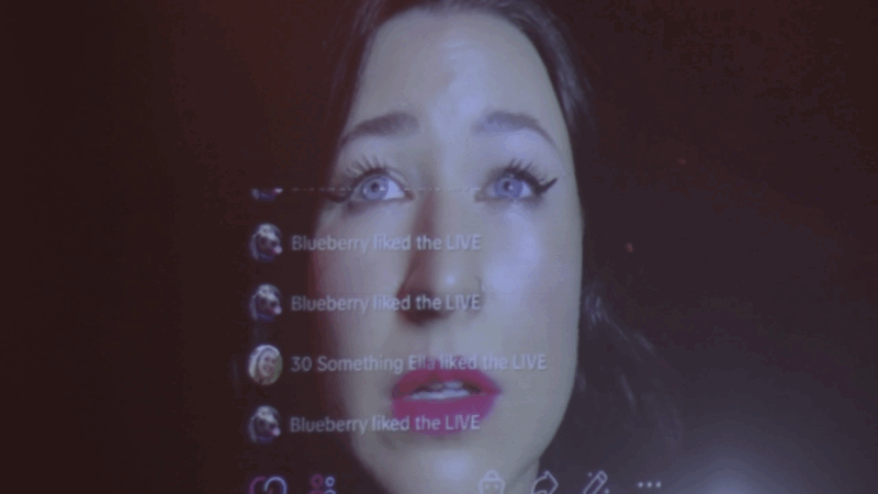 Vlose-up of a person's face. They have dark hair and wear red lipstick. A computer screen is reflected on their face