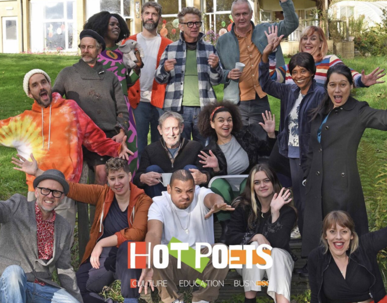 Group of diverse adults posing happily outdoors on a sunny day with greenery and buildings in the background.