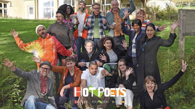 Group of diverse adults posing happily outdoors on a sunny day with greenery and buildings in the background.
