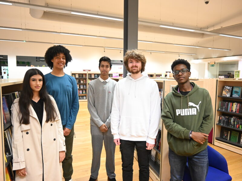 A group of diverse young people stand in a library