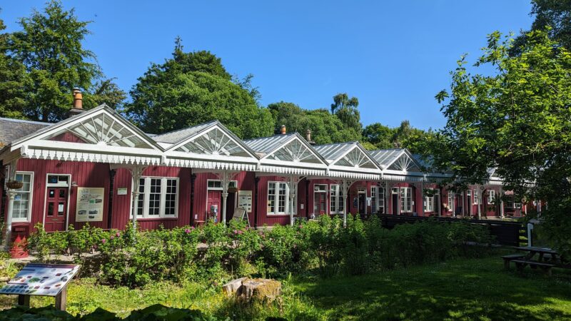 Victorian railway station with charming red cottages with white trim under a clear blue sky surrounded by lush green trees and bushes.