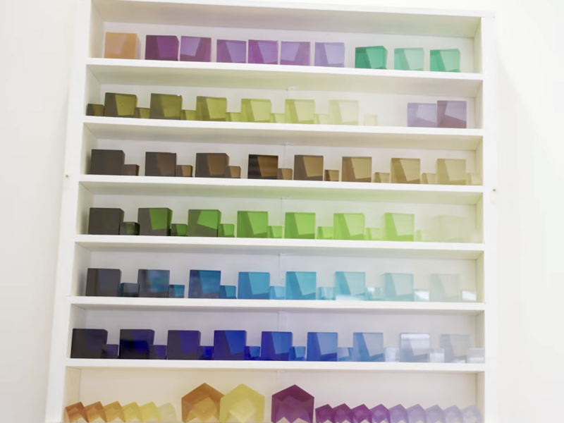 Glass tiles in various colours stacked on a white shelving unit.